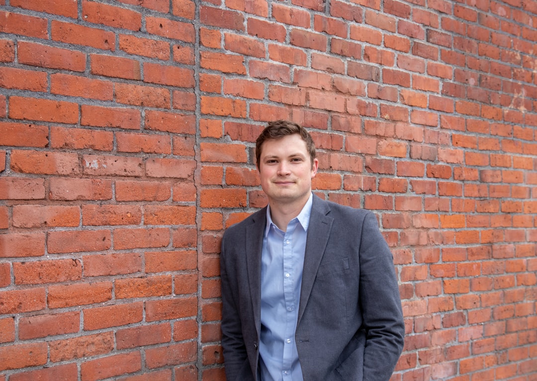 verify support animal — man in black suit jacket standing beside brown brick wall